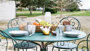 Una mesa al aire libre con una cesta de frutas, un vaso de leche y una botella de agua.