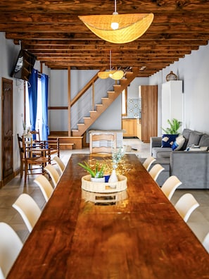 A spacious dining area with a long wooden table, a staircase, and a living area with a sofa and a potted plant. - Maison 'Le Figuier' with Shared Garden and Wi-Fi (Chenou)