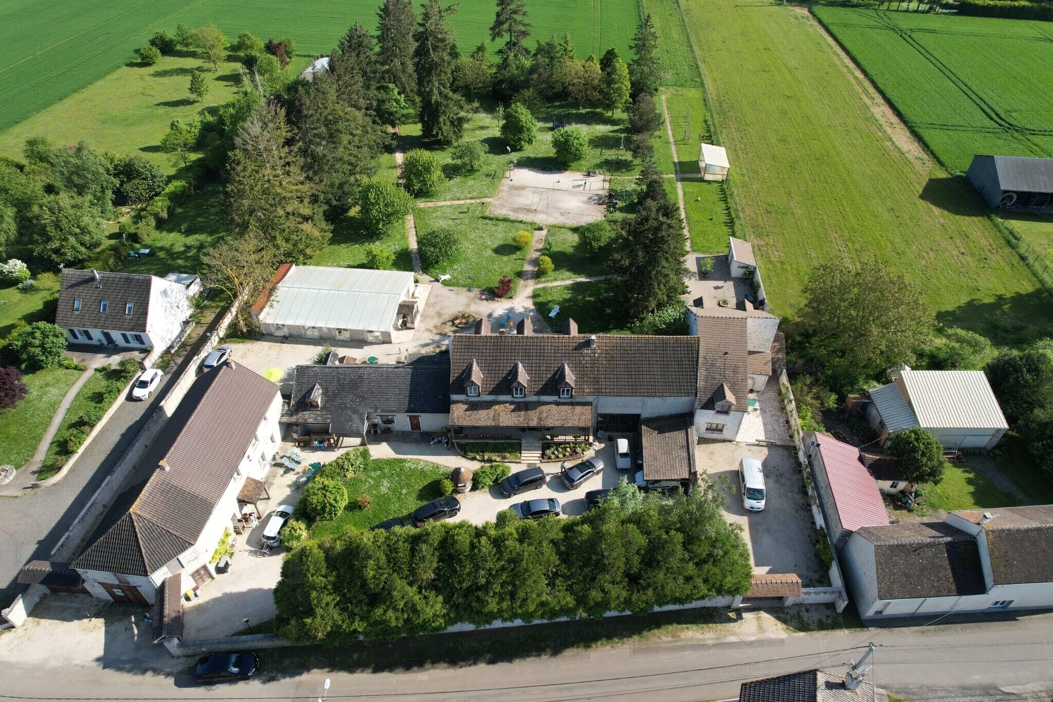 Oversigtsbillede af et boligområde med flere huse, en parkeringsplads og grønne marker omkring.