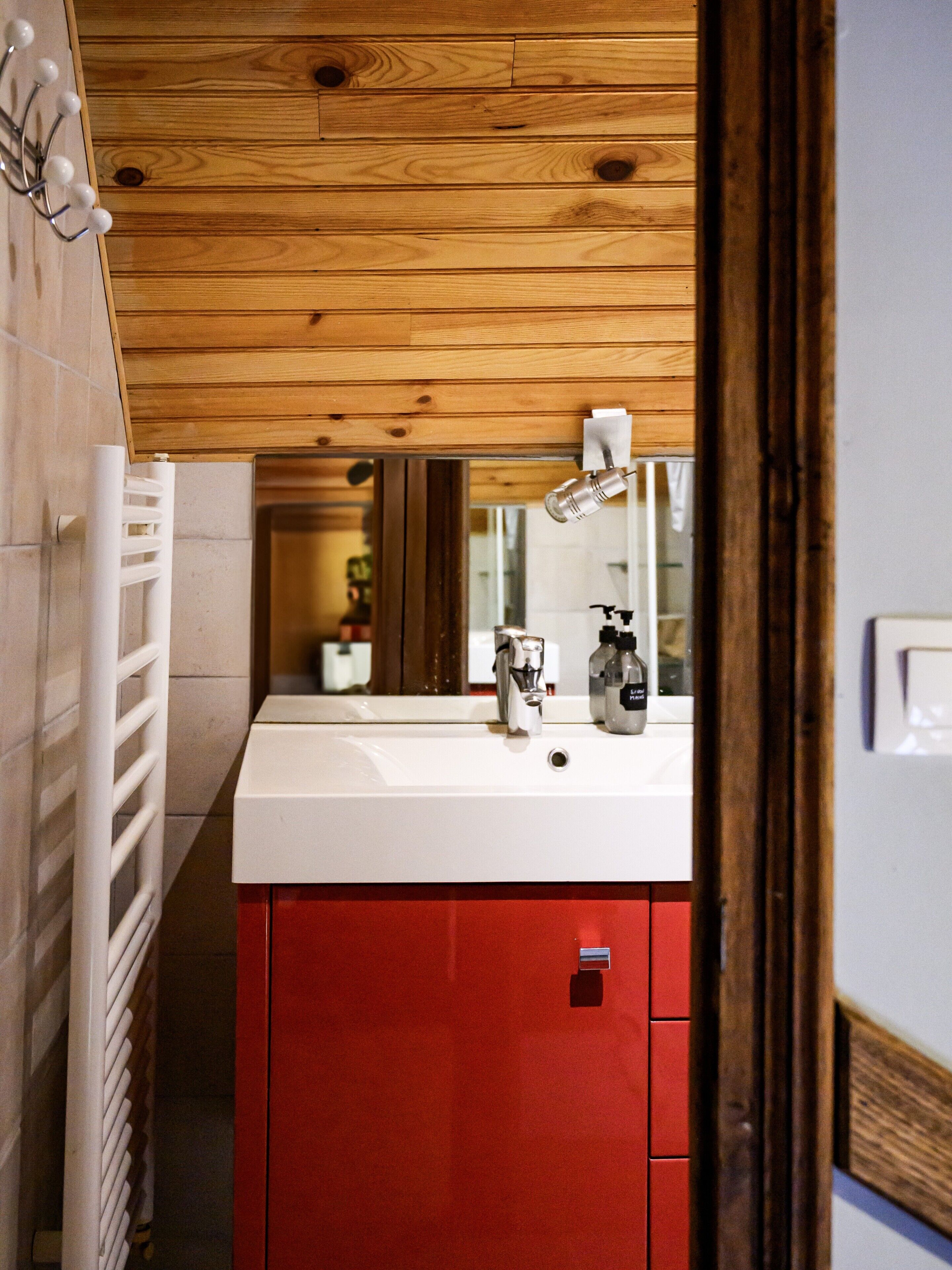 A bathroom with a wooden ceiling, a white sink, a red cabinet, and a mirror.