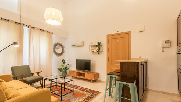 A living room with a sofa, chairs, a TV, a coffee table, and a small bar area.