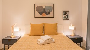 A neatly made bed with a patterned bedspread, two bedside lamps, and a framed abstract artwork on the wall.
