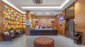 A hotel lobby with a reception desk, bookshelves, a tufted ottoman, and a trash bin.
