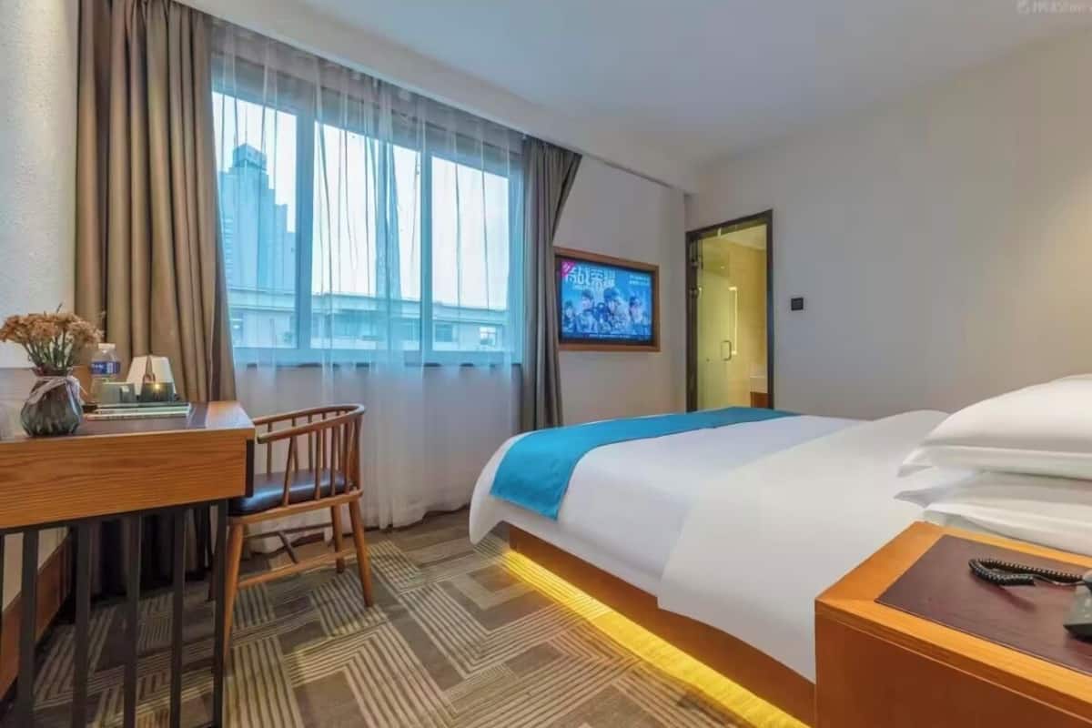 Ein Hotelzimmer mit Bett, Schreibtisch, Stuhl, Fernseher und einem Fenster mit Vorhängen.