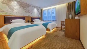 A hotel room with two beds, a large world map on the wall, a TV, and a wooden desk.