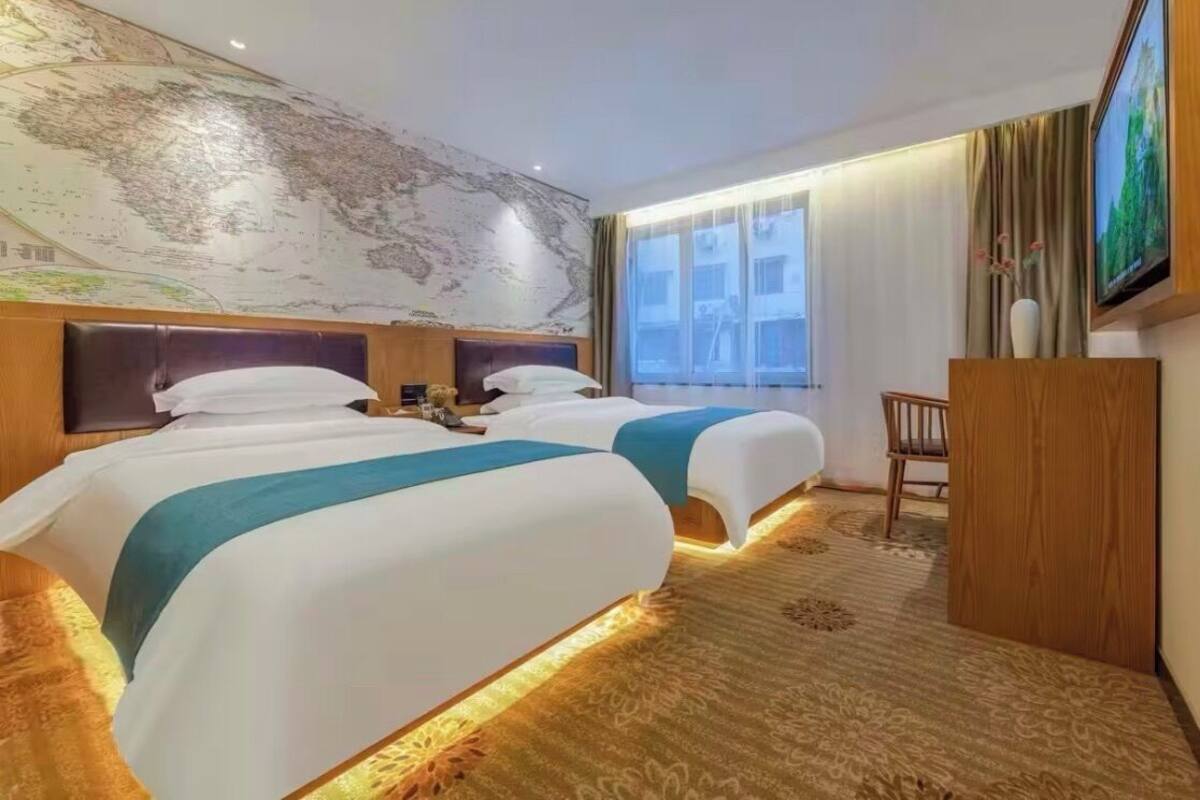 Ein Hotelzimmer mit zwei Betten, einer großen Weltkarte an der Wand, einem Fernseher und einem Holztisch.