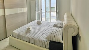 Un dormitorio con una cama, una araña, un radiador y vistas a través de un ventanal.