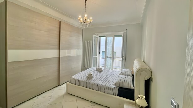 Un dormitorio con cama, una araña y una puerta corredera, con vistas a través de la puerta.
