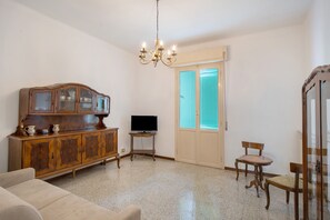 Un salon comprenant un meuble en bois, un téléviseur, un lustre et une porte avec des stores.