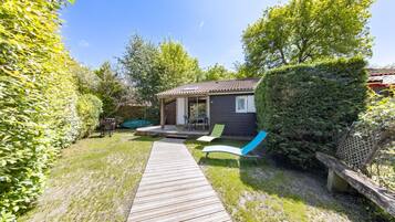 A wooden deck leading to a house with a patio area, a small garden, and a bench.