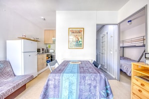 A compact room with a bed, a sofa, a kitchenette, and a door leading to a balcony. - Comfortable Chalet Near the Beach and Marina – Garden, Parking, Leisure Facilities (Hourtin)