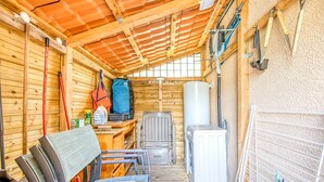 A compact, wooden cabin with a tiled roof, a washing machine, a chair, and a drying rack.
