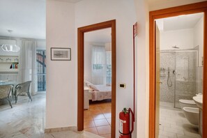 A hotel room with a bed, a bathroom with a shower, and a dining area with a table and chairs. - Apartment 'Riviera' with Balcony, Wi-Fi and Air Conditioning (Sanremo)