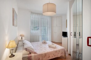 A bedroom with a bed, bedside lamp, and a television on a small cabinet. - Apartment 'Riviera' with Balcony, Wi-Fi and Air Conditioning (Sanremo)