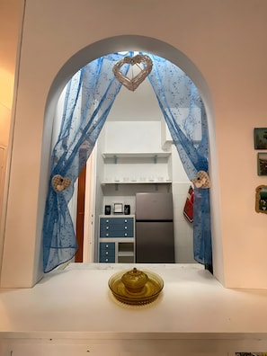 A kitchen with a refrigerator, cabinets, and a window with blue curtains.
