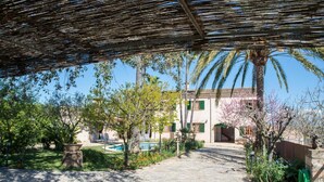 A covered outdoor area with a stone pathway, a pool, and a building with a tiled roof. - Villa 'Vernissa 10p' with Mountain View (Santa Margalida)