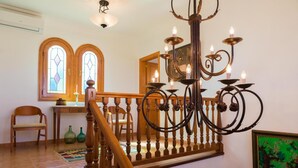 A staircase with wooden balusters, a chandelier with multiple candle-like lights, and a stained glass window. - Villa 'Vernissa 10p' with Mountain View (Santa Margalida)