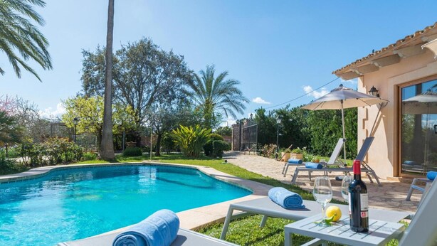 A swimming pool with lounge chairs, a bottle of wine, and a lemon on a table. - Villa 'Vernissa 10p' with Mountain View (Santa Margalida)