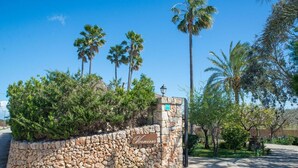 A stone wall with a sign reading 'Vernissa' and palm trees in the background. - Villa 'Vernissa 10p' with Mountain View (Santa Margalida)