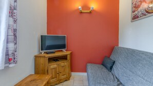A living room with a television on a wooden cabinet, a grey sofa, and a red accent wall. - Apartment 'A1 Renard' with Mountain View, Shared Garden and Wi-Fi (Le Bourg-d'Oisans)