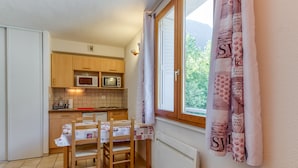 A compact kitchen with wooden cabinets, a microwave, and a table with chairs. - Apartment 'A1 Renard' with Mountain View, Shared Garden and Wi-Fi (Le Bourg-d'Oisans)