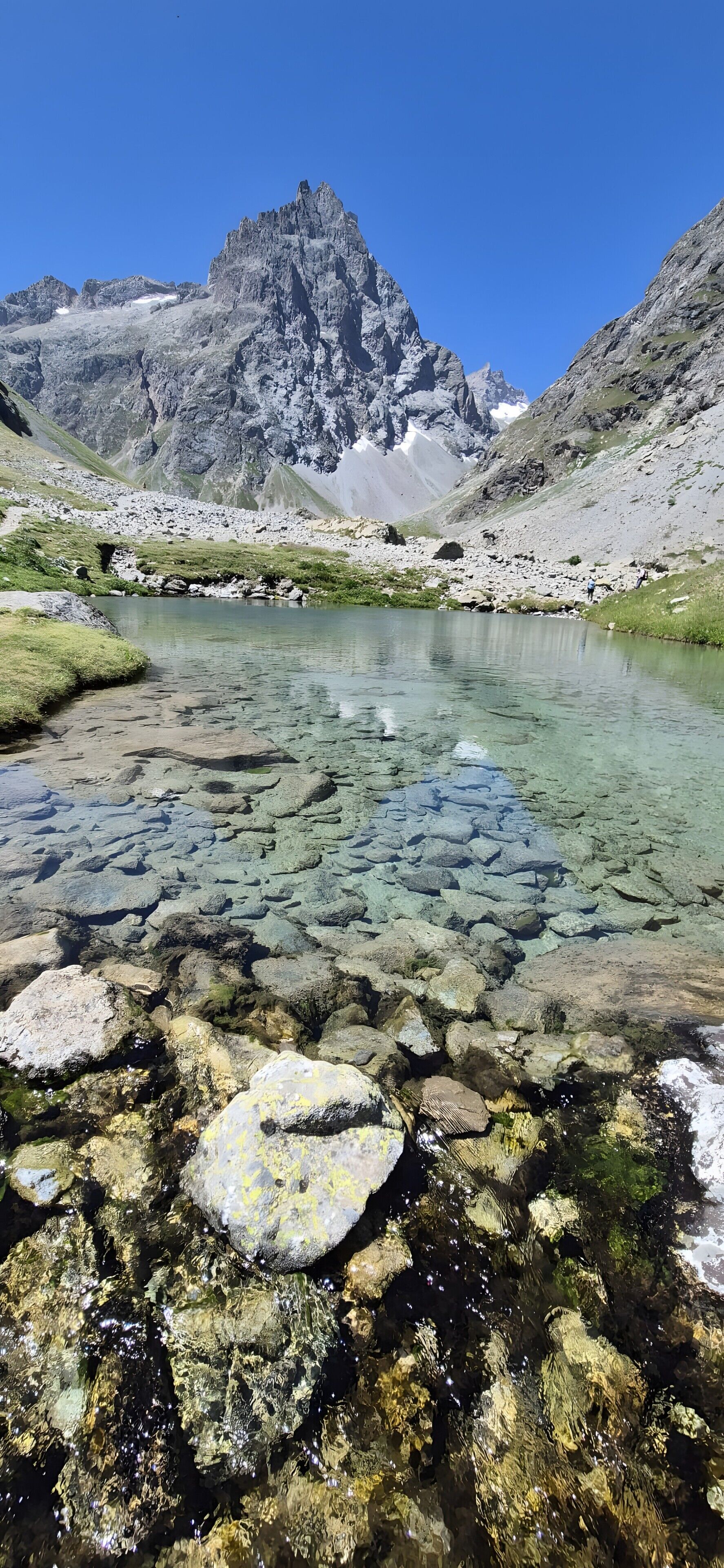 Ein klarer Bergsee mit steinigen Ufern und einem markanten Berggipfel im Hintergrund.