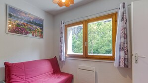 A room with a red sofa, a window with curtains, a radiator, and a painting on the wall. - Apartment 'B3 Chamois' with Mountain View, Shared Garden and Wi-Fi (Le Bourg-d'Oisans)