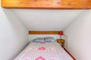 A bedroom with a sloped ceiling, a bed with a checkered bedspread, two pillows, a bedside table with a lamp, and a wooden headboard. - Apartment 'B3 Chamois' with Mountain View, Shared Garden and Wi-Fi (Le Bourg-d'Oisans)