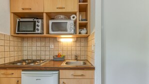 Een kleine keuken met een fornuis, magnetron en kleine koelkast.