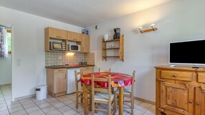 Une cuisine compacte comprenant une table à manger, des placards en bois, un four à micro-ondes et un téléviseur.