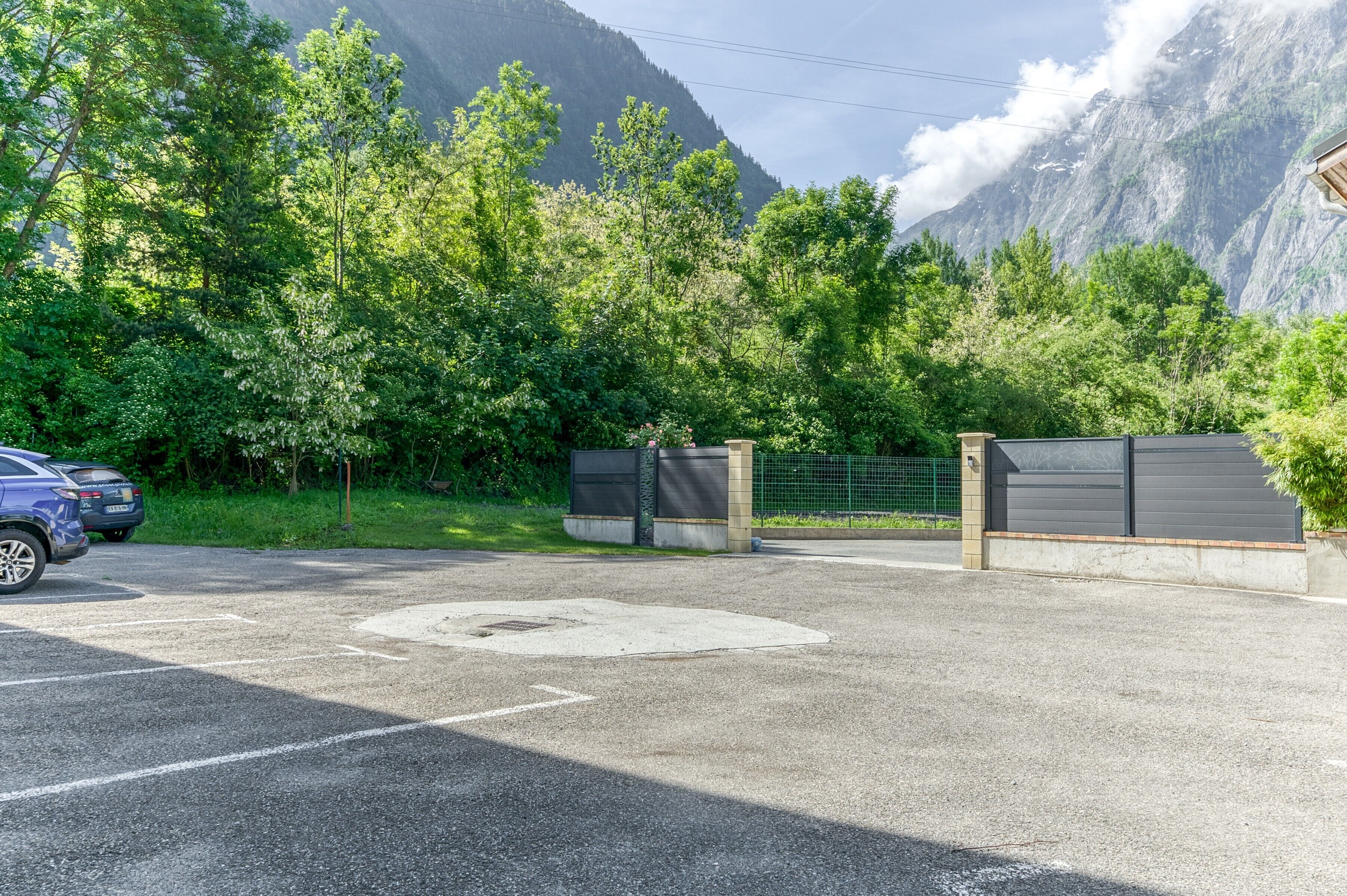 A parking area with a mountain backdrop, a gated entrance, and a blue car parked.