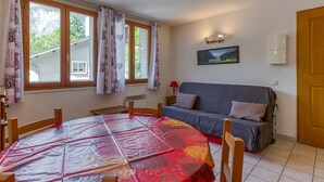 Une pièce comprenant une table à manger, un canapé, une fenêtre avec des rideaux, un tableau accroché au mur et une porte.