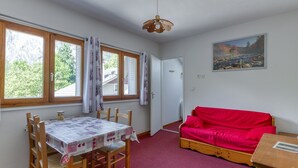 Ett rum med ett matbord, stolar, en röd soffa, en tavla och en dörr som leder till ett annat rum.