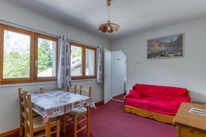 A room with a dining table, chairs, a red sofa, a painting, and a door leading to another room.