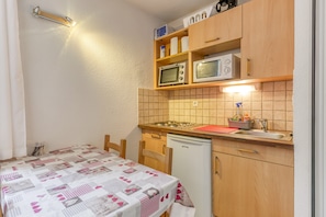 A compact kitchen with a microwave, stove, and sink. There is a table with a patterned tablecloth.
