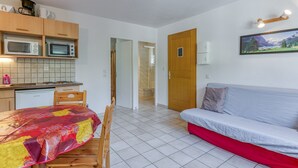 A compact living space with a kitchenette, a dining area, and a sofa. - Apartment 'B4 Ecureuil' with Mountain View, Shared Garden and Wi-Fi (Le Bourg-d'Oisans)