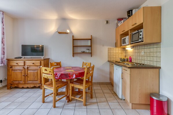 A compact kitchen with wooden cabinets, a dining table with chairs, a microwave, and a television.