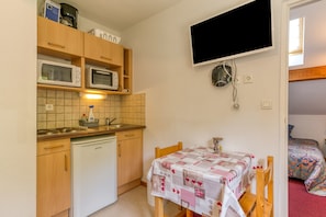 A compact kitchen with a microwave, toaster, and sink, a table with a patterned tablecloth, and a TV mounted on the wall.