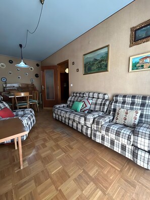 A living room with a checkered sofa, a wooden dining table, and a dining area. - Apartment 'Clementina' with Air Conditioning (Sanremo)