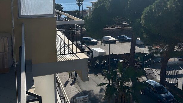Un immeuble à plusieurs étages doté d’un balcon donnant sur un parking et offrant une vue sur la mer.