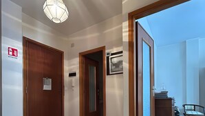 Un couloir doté d’un sol en marbre, de portes en bois, d’un luminaire suspendu et offrant une vue sur l’extérieur.
