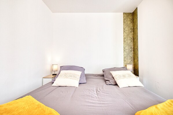 A bedroom with a bed, two pillows, a nightstand, a lamp, and a patterned wall.