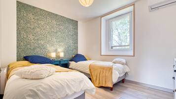 Slaapkamer met twee bedden, een raam, een wand met bloemenprint en een plafondlamp.