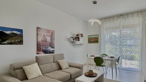 Un salon moderne comprenant un canapé d’angle, une table basse, un coin repas avec une table et des chaises, et une grande fenêtre offrant une vue dégagée.