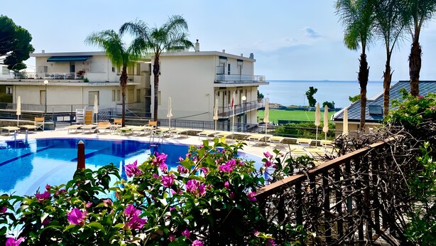 Un espace piscine avec des chaises longues, un bâtiment doté de balcons et une vue sur la mer.