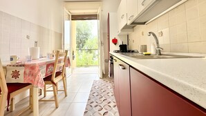 A kitchen with a dining area, a balcony, and a view of greenery. - Apartment 'Alice' with Sea View, Balcony and Wi-Fi (Sanremo)