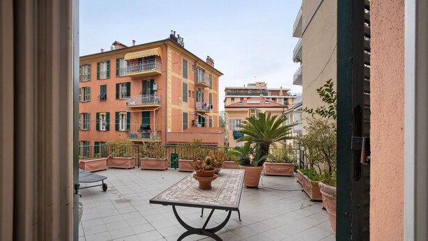 A courtyard with a tiled floor, a table, potted plants, and buildings in the background. - Apartment 'La Terrazza Di Sabrina' with Private Terrace, Balcony and Wi-Fi (Sanremo)
