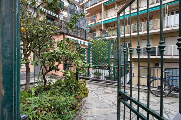 Une cour avec un chemin en pierre, des rampes en métal vert, un vélo et un bâtiment doté de balcons.