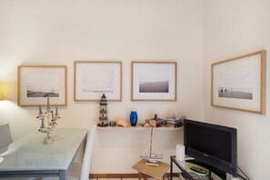 Une pièce avec une table en verre, un téléviseur, des tableaux encadrés accrochés au mur et une petite étagère sur laquelle sont disposés divers objets.