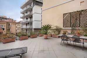 Une terrasse sur le toit, avec une table et des chaises, des plantes en pot et une vue sur les bâtiments voisins.